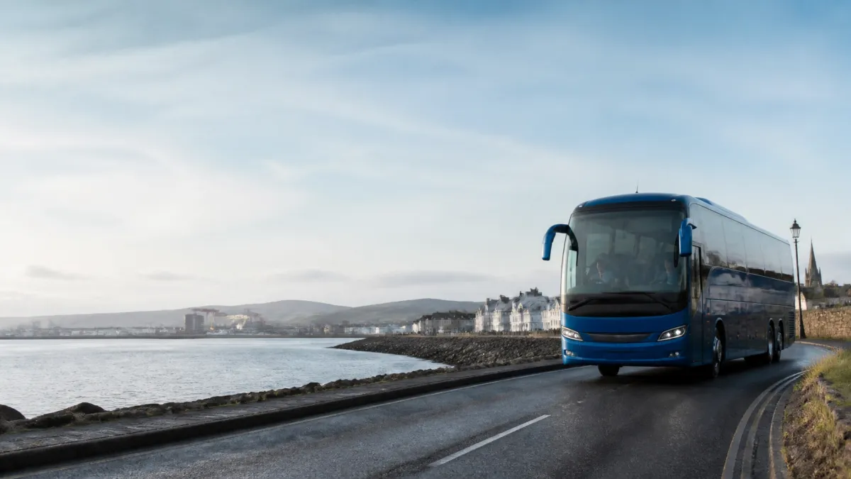 A modern blue coach travelling along a coastal road in Northern Ireland